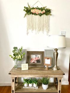 a wooden table topped with pictures and plants next to a wall hanging on the wall