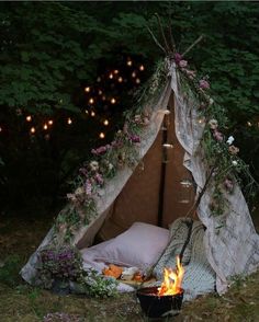 a teepee in the woods with flowers on it and lights hanging from the ceiling