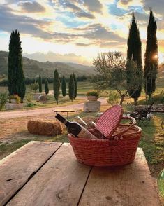 a wicker basket filled with wine bottles sitting on top of a wooden picnic table