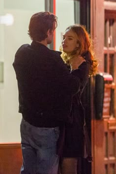 a man and woman standing next to each other in front of a building at night