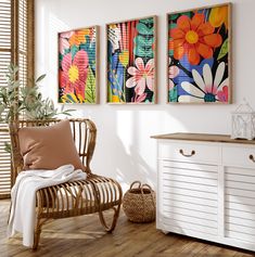 three paintings hang on the wall next to a chair and sideboard in a room