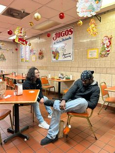 a man and woman sitting at a table in a fast food restaurant with orange chairs