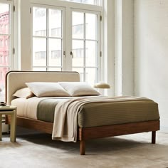 a bed sitting in front of a window next to a table with a lamp on it