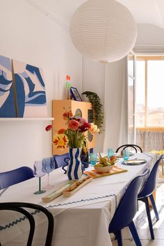 a dining room table is set with blue chairs and white linens, along with colorful art on the wall