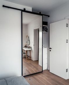 an open door leading to a bedroom with white walls and wood flooring, in front of a bed