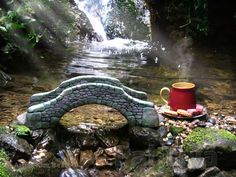 a tea cup sits on top of a stone bench next to a stream and waterfall