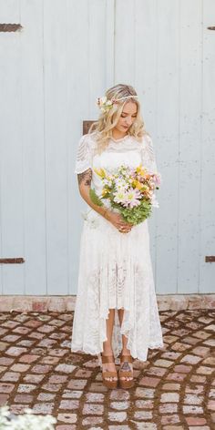 a woman standing in front of a white door holding a bouquet of flowers and wearing sandals