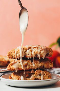 a spoon drizzling icing onto some food on a plate with other foods in the background