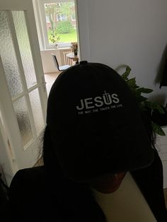 a person wearing a black hat with the word jesus on it in front of a door