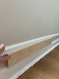 someone is holding the edge of a piece of wood on top of a white wall