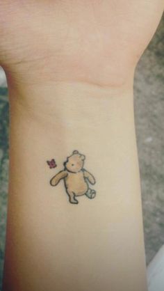 a small tattoo on the wrist of a girl with a teddy bear holding a flower