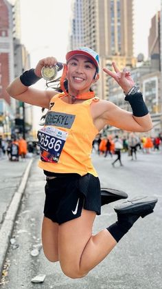 a woman is jumping in the air with her hands up while wearing an orange shirt and black shorts