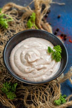 a black bowl filled with white sauce and garnished with parsley