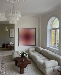 a living room filled with furniture and a chandelier hanging from the ceiling next to a large window