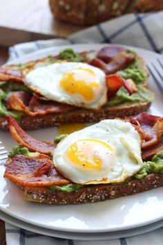 two eggs are on toast with avocado and bacon in the middle, sitting on a white plate