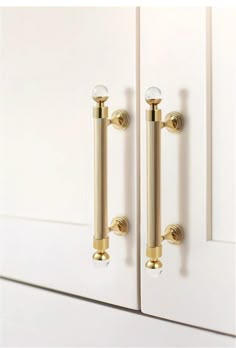 an image of a door handle on the front of a white cabinet with gold handles