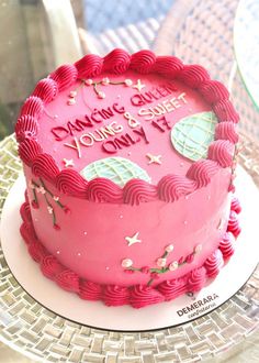 a pink birthday cake sitting on top of a table next to a plate with a knife and fork