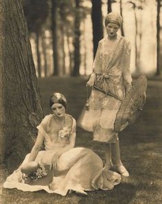 an old photo of two women sitting next to each other in front of a tree