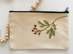 a beaded necklace is hanging from a zippered pouch with embroidered berries and leaves on it