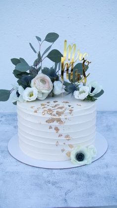 a white cake with gold letters and flowers on top