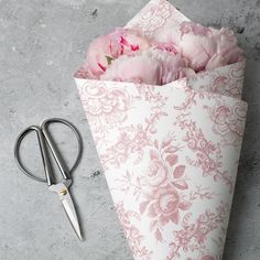 a bunch of pink flowers in a paper bag next to scissors and a pair of scissors