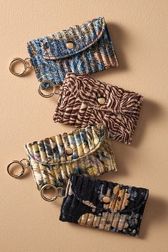 three purses with key chains hanging from them on a beige wall, one is blue and the other is brown