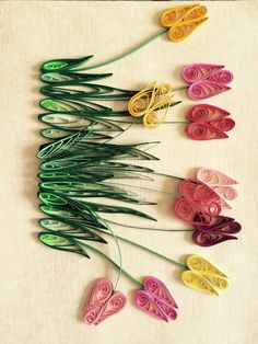 colorful paper flowers are arranged on a white surface with green stems in the foreground