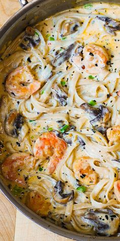 a pan filled with pasta and shrimp on top of a wooden table