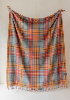 an orange and blue plaid blanket with fringes on the bottom, hanging from a white wall