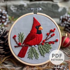 a red bird sitting on top of a tree branch with berries and pine cones around it