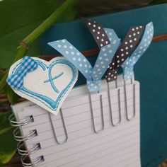 some paper clips are attached to a clipboard with a heart on it and a ribbon in the shape of a bow