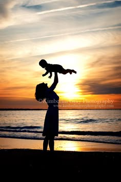 a man holding a baby up in the air on top of a beach at sunset