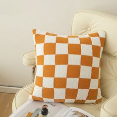 an orange and white checkered pillow sitting on top of a chair next to a magazine