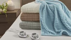 an electric heated blanket and earbuds are on a bed with folded towels, headphones, and plant in the background