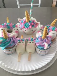 cupcakes decorated with unicorn faces and rainbow icing are on a paper plate