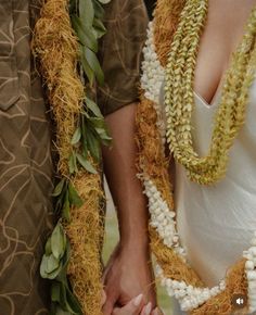 two people holding hands and wearing leis