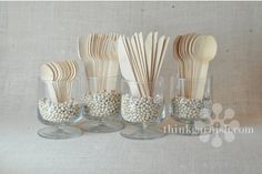 there are many wooden spoons in the glass cups with white beads on each one