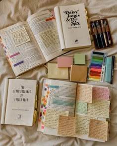 there are many different types of books and pens on the bed with paper notes attached to them