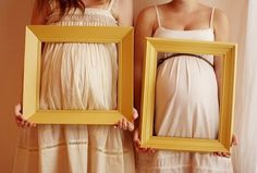 two pregnant women holding framed pictures in front of their faces, one is wearing a white dress