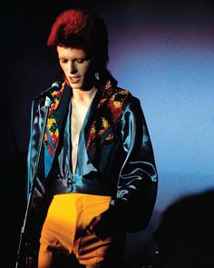 a man with red hair wearing a black jacket and yellow pants standing in front of a microphone