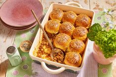 a casserole dish filled with sliders next to a potted plant on a table