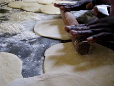 a person is kneading dough on top of floured pizza crusts in an industrial kitchen