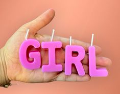 the word girl spelled out with candles in front of a hand holding it up against a pink background