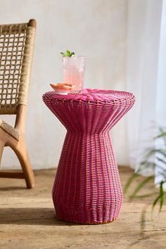 a wicker table with a drink on it next to a chair and potted plant