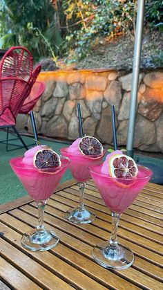 three glasses filled with fruit sitting on top of a wooden table