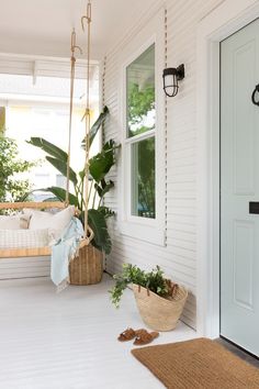 a porch with white walls and plants on the floor, hanging from a swing bed