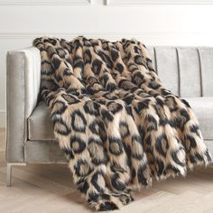 an animal print blanket on a couch in a room with white walls and wood flooring