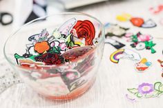 a bowl filled with lots of stickers sitting on top of a table next to scissors