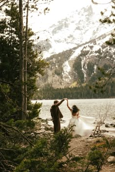 a bride and groom standing in front of a mountain lake