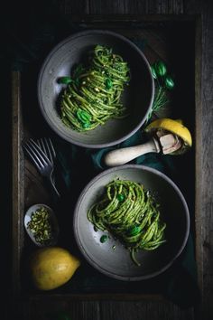 two bowls filled with green pasta next to lemons